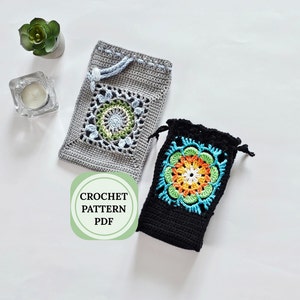 May include: Two crocheted drawstring bags with colorful floral designs. The bag on the left is gray with a green, blue, and white floral design. The bag on the right is black with a green, orange, yellow, and white floral design. The text "CROCHET PATTERN PDF" is on a green circle.