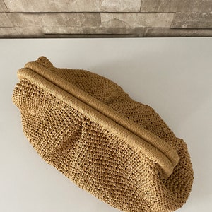 May include: A tan woven straw clutch bag with a top closure.