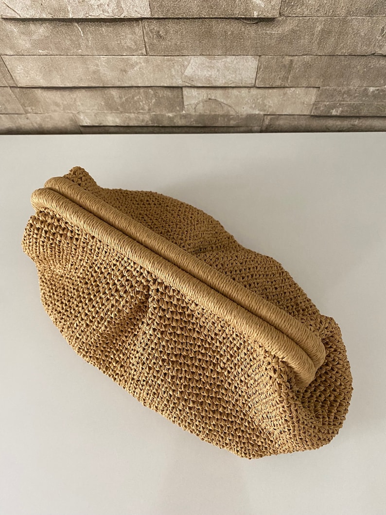 May include: A tan woven straw clutch bag with a top closure.