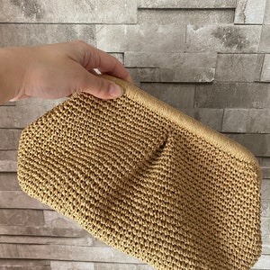 May include: A tan woven straw clutch bag with a slightly textured surface.