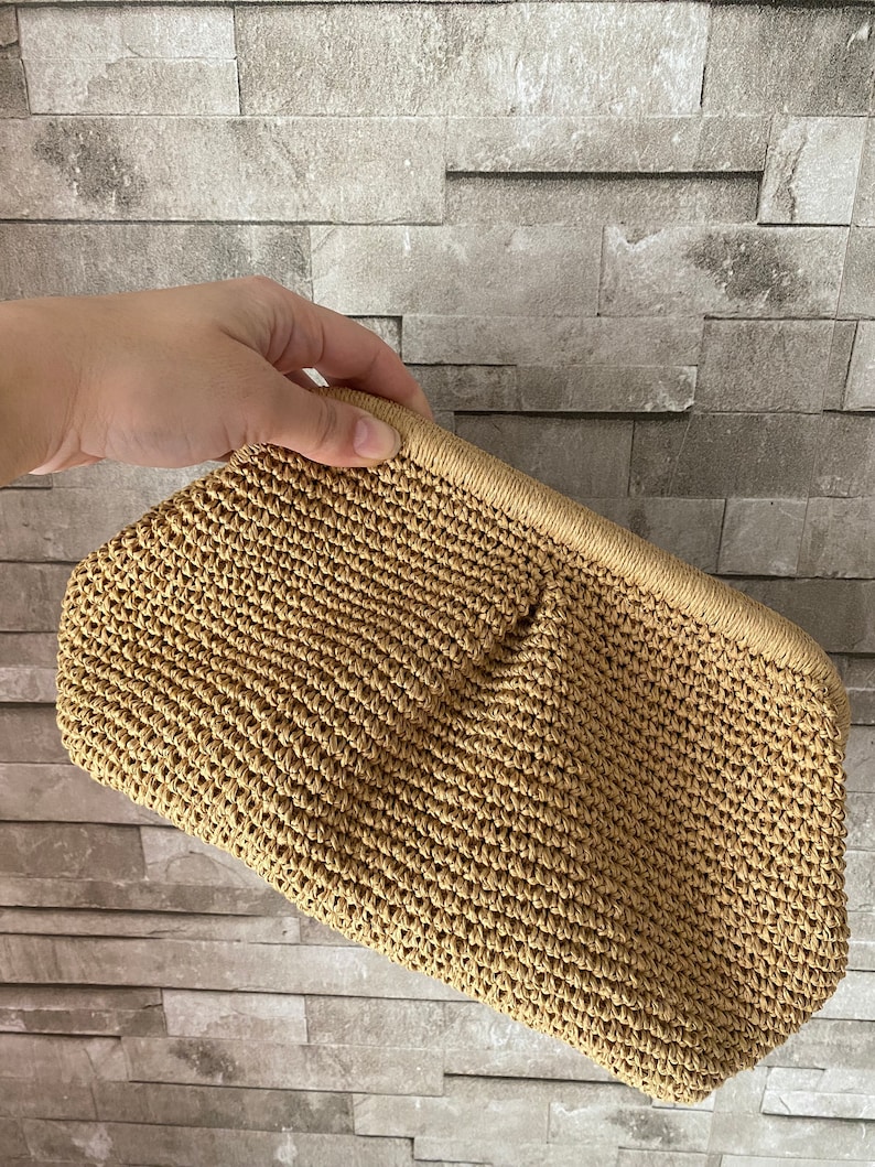 May include: A tan woven straw clutch bag with a slightly textured surface.