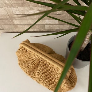 May include: A tan crocheted clutch bag with a woven texture. The bag has a simple design and a smooth, flat surface.