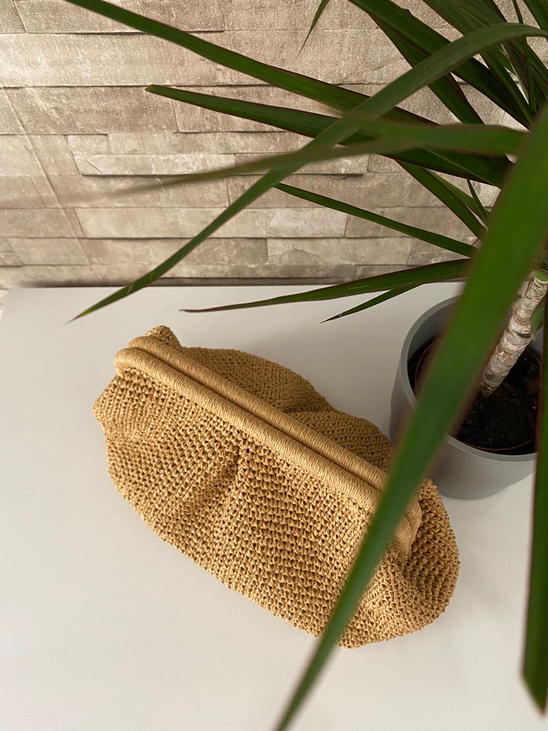 May include: A tan crocheted clutch bag with a woven texture. The bag has a simple design and a smooth, flat surface.