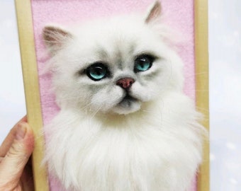 Pode incluir: Um gato branco e felpudo de feltro com olhos azuis em uma moldura rosa.