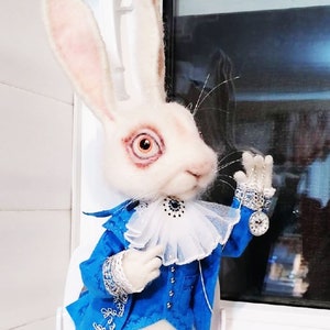 Könnte beinhalten: Ein weißes Kaninchen, das eine blaue Jacke mit silbernen Verzierungen und einen weißen Rüschenkragen trägt. Das Kaninchen hält eine Taschenuhr mit einer silbernen Kette.