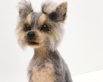 May include: A needle-felted sculpture of a small dog with long, textured fur in shades of gray, tan, and brown. The dog has upright ears, dark eyes, and a black nose, sitting in an alert posture with its front paws planted firmly forward.