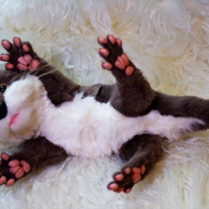 Op de afbeelding: Een pluche otter met bruine vacht, een witte buik en roze pootjes. De otter ligt op zijn rug met zijn poten in de lucht.