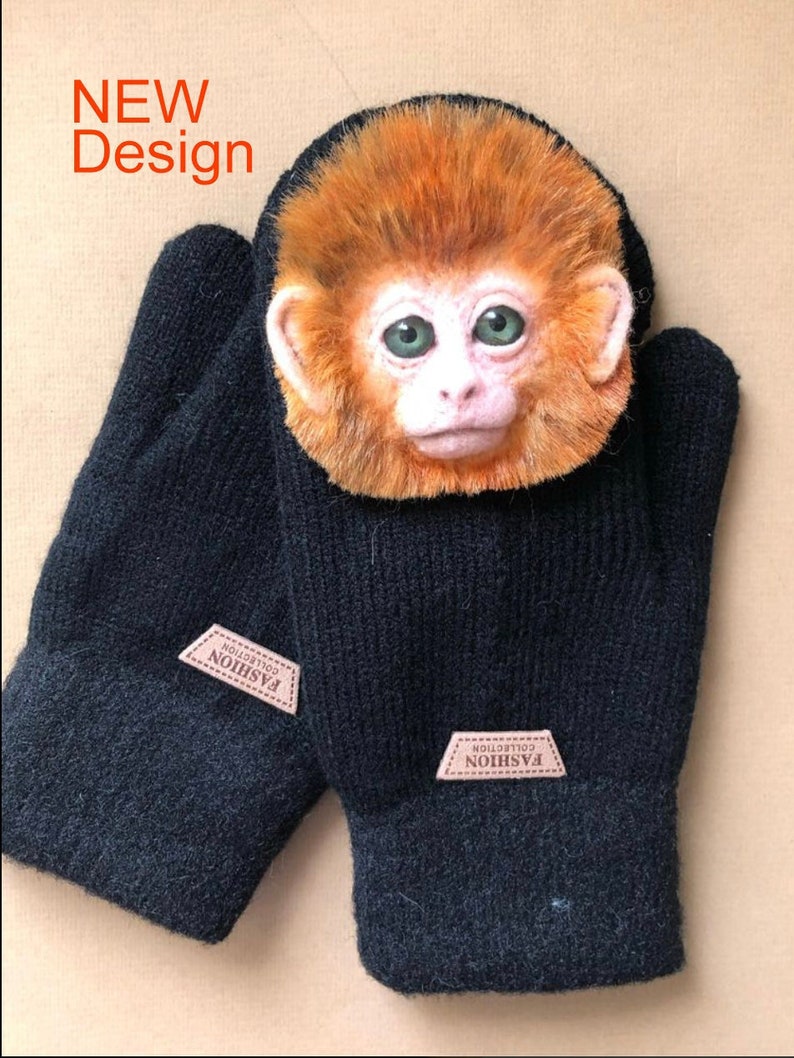 Puede incluir: Un par de guantes de punto negros con un parche de cuero marr&oacute;n que dice "FASHION COLLECTION" en cada guante. El guante derecho tiene una peque&ntilde;a cara de mono de aspecto realista unida a &eacute;l.