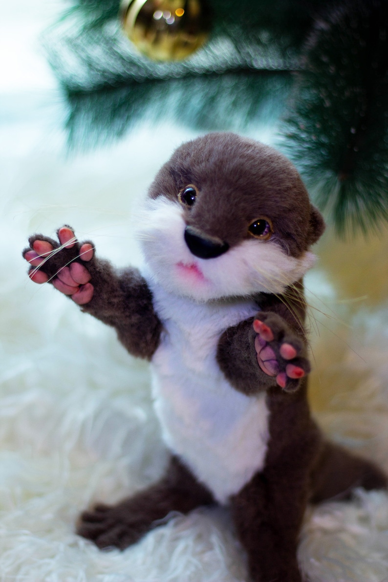 Op de afbeelding: Een pluche otter speelgoed met bruine vacht, een witte borst en roze pootjes. De otter staat op een wit, pluche oppervlak en heeft een speelse uitdrukking.