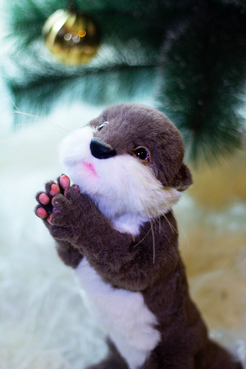 Op de afbeelding: Een pluche bruine en witte otter met een witte borst en een roze neus. De otter houdt zijn poten bij elkaar in een gebedshouding.