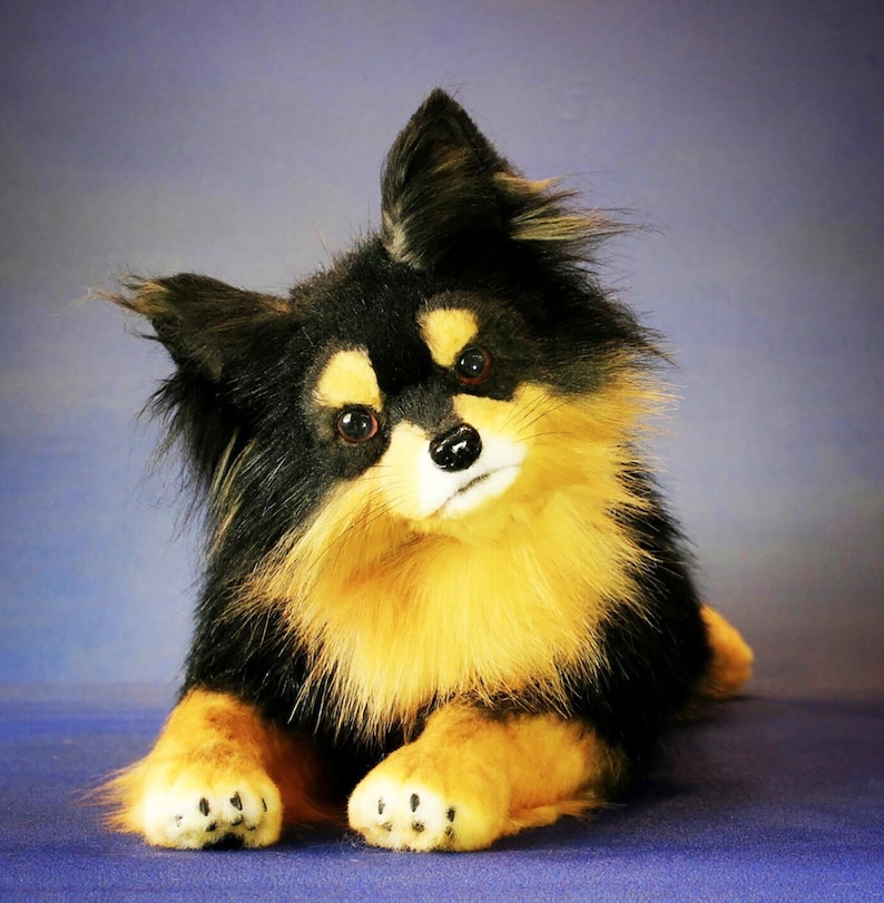 May include: A black and tan plush dog with long fur and large brown eyes. The dog is lying on its side with its head tilted to the side.