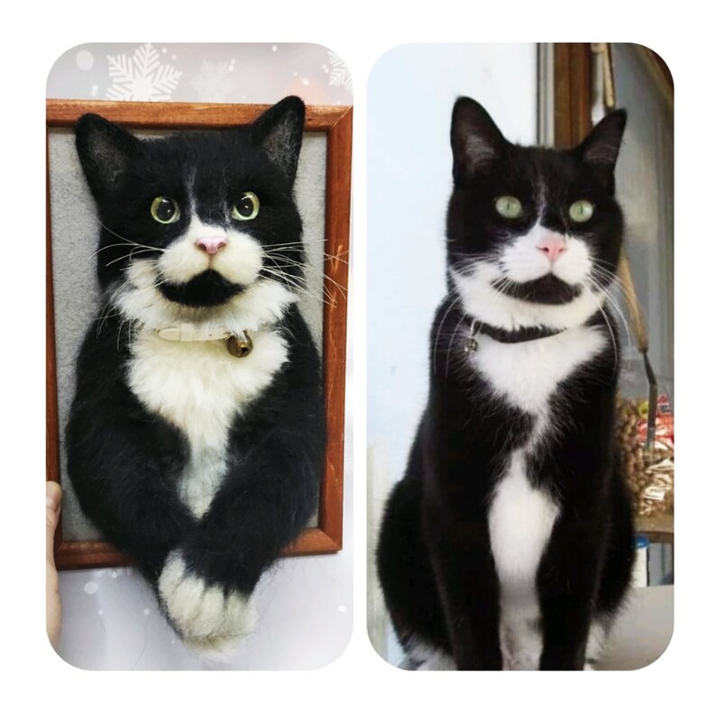 May include: A black and white cat with green eyes and a pink nose. The cat is wearing a collar with a bell. The image shows a framed felted portrait of the cat next to a photo of the cat.