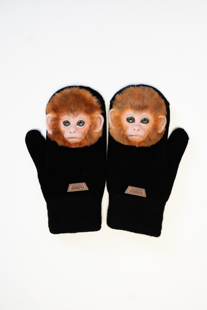 Puede incluir: Un par de guantes de punto negros con una cara de mono en cada uno. Las caras de mono son marrones y tienen ojos verdes. Los guantes tienen una etiqueta de cuero marr&oacute;n que dice "FASHION COLLECTIBLES".