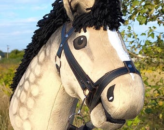 May include: A plush hobby horse head with a black mane and a black leather bridle. The horse has a light tan body with darker spots and a white stripe down the face. The toy is designed for children.