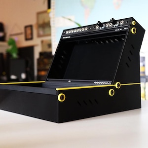 Può includere: Un case per sintetizzatore modulare nero con pannello superiore inclinato, caratterizzato da accenti giallo brillante lungo i bordi e supporti circolari per viti. L'unità presenta una serie di jack di ingresso e manopole di controllo.