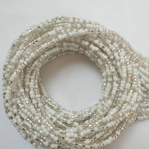 Op de afbeelding: Een opgerolde bundel witte en zilveren zaadkralen. De kralen zijn klein, cilindrisch en dicht op elkaar gepakt. Ze hebben een combinatie van ondoorzichtig wit en metallic zilver, geschikt voor sieraden of knutselprojecten.