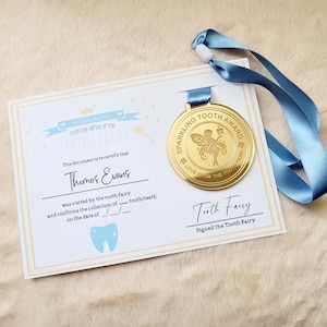 May include: A gold-colored medal with a blue ribbon. The medal features a fairy with wings and a tooth. The text on the medal reads "Sparkling Tooth Award Love From The Tooth Fairy". A certificate with the text "From the office of the Tooth Fairy" is also shown.