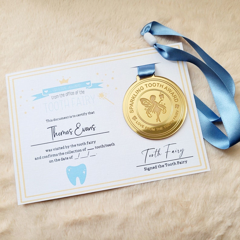 May include: A gold-colored medal with a blue ribbon. The medal features a fairy with wings and a tooth. The text on the medal reads "Sparkling Tooth Award Love From The Tooth Fairy". A certificate with the text "From the office of the Tooth Fairy" is also shown.