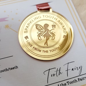 May include: A gold-colored medal with a tooth fairy design. The medal says "Sparkling Tooth Award" and "Love from the Tooth Fairy".