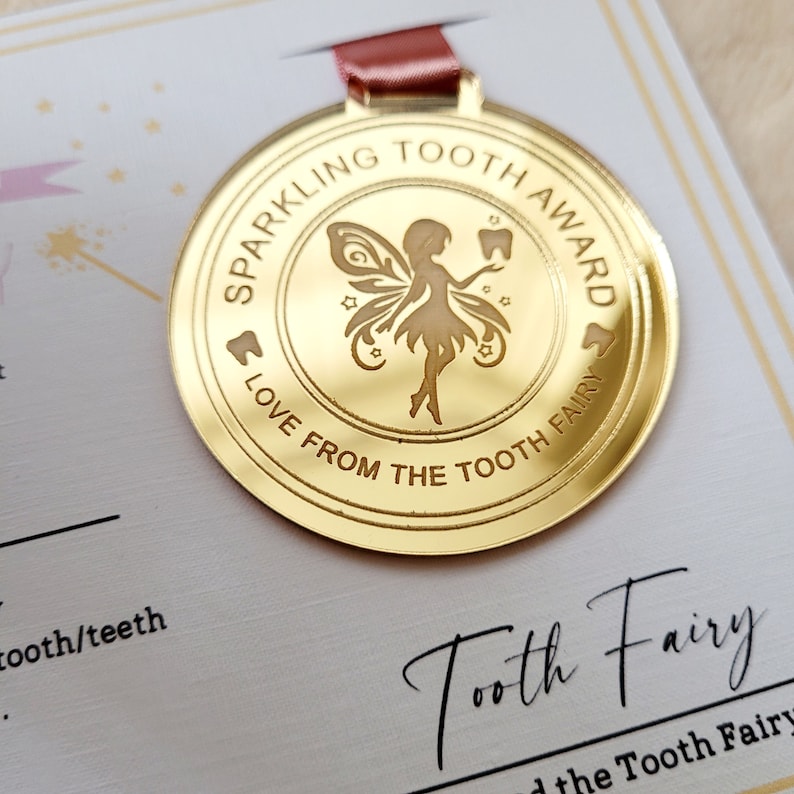 May include: A gold-colored medal with a tooth fairy design. The medal says "Sparkling Tooth Award" and "Love from the Tooth Fairy".