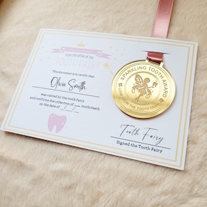May include: A gold-colored medal with a tooth fairy design and the text "Sparkling Tooth Award Love from the Tooth Fairy". The medal is attached to a pink ribbon and a white certificate with the text "From the office of the Tooth Fairy" and "This document is to certify that Olivia Smith was visited by the tooth fairy and confirms the collection of tooth/teeth on the date of __/__/__".