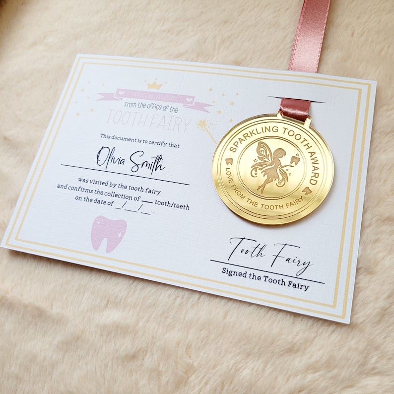 May include: A gold-colored medal with a tooth fairy design and the text "Sparkling Tooth Award Love from the Tooth Fairy". The medal is attached to a pink ribbon and a white certificate with the text "From the office of the Tooth Fairy" and "This document is to certify that Olivia Smith was visited by the tooth fairy and confirms the collection of tooth/teeth on the date of __/__/__".