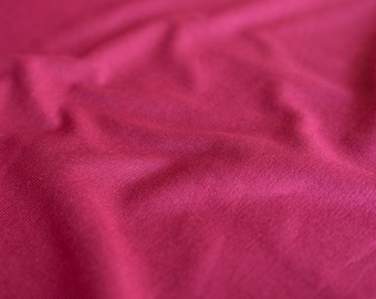 May include: Close-up of a smooth, deep pink fabric with a subtle texture. The fabric is wrinkled and folded, creating a soft, flowing look.