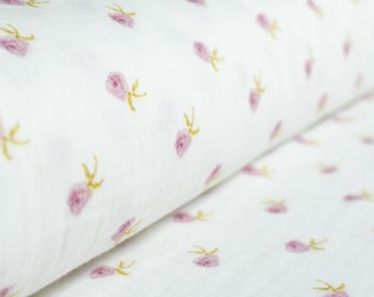 May include: White fabric with a repeating pattern of small pink roses and yellow stems. The fabric is soft and appears to be lightweight, suitable for various sewing projects. The roses are evenly spaced across the surface.