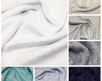 May include: A collage of close-up shots of soft, plush fabric in various colors. The colors include white, cream, gray, teal, light blue, and navy. The fabric has a textured, fuzzy appearance, suggesting a cozy material.