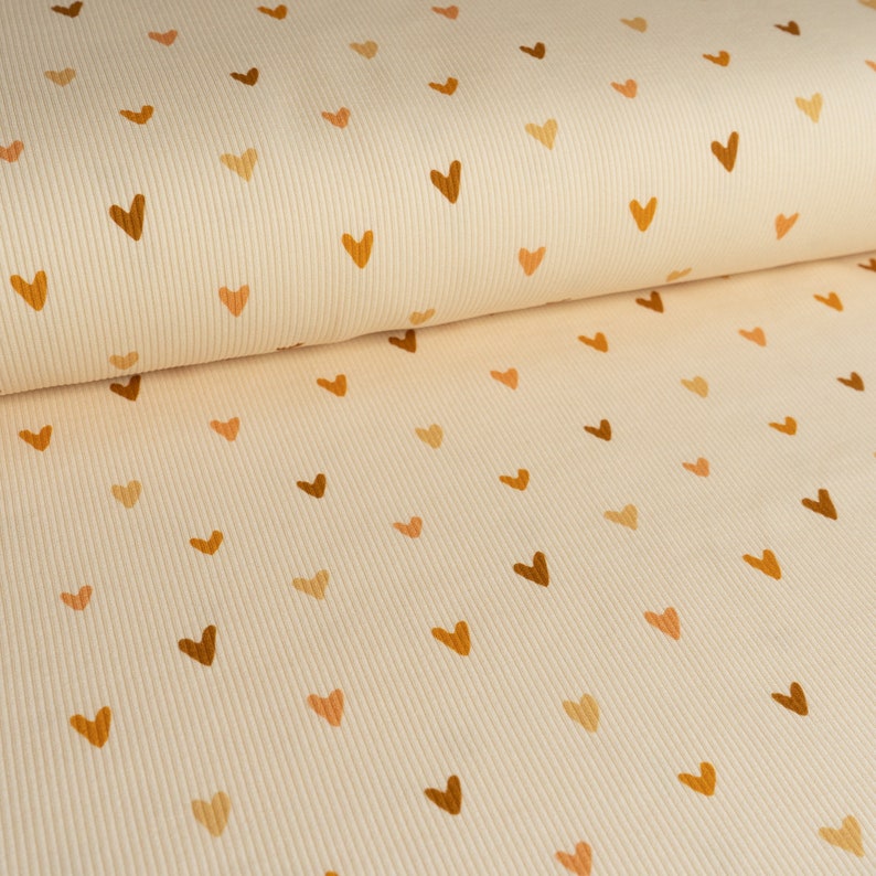 May include: Cream-colored ribbed fabric with a repeating pattern of small brown, orange, and peach hearts.