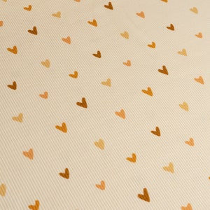 May include: A beige fabric with a repeating pattern of brown hearts.