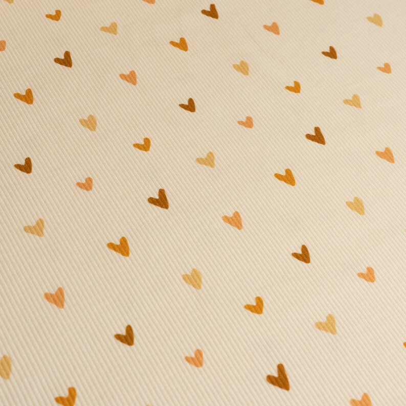 May include: A beige fabric with a repeating pattern of brown hearts.