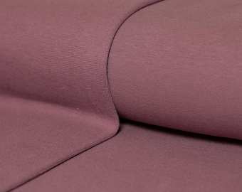 May include: Close-up of a soft, mauve-colored fabric with a subtle ribbed texture. The fabric is folded over itself, creating a smooth, curved surface.