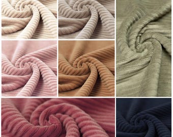 May include: A collection of corduroy fabric swatches featuring a distinct ribbed texture. The colors include cream, beige, olive green, light pink, tan, dusty rose, and navy blue, each arranged in a spiral pattern to highlight the fabric's surface.