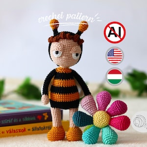 May include: A handmade crochet bee doll with a black and orange striped body, standing next to a colorful crochet flower. The doll has a light brown head, antennae, and orange feet. The words "crochet pattern" are written above the doll.