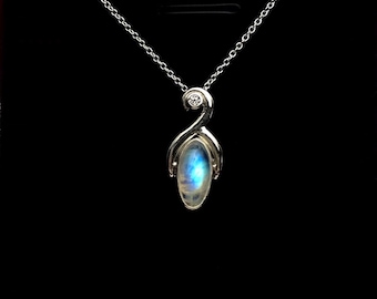 May include: A silver necklace with a pendant featuring a blue and white oval gemstone. The pendant has a unique, curved design with a small, round accent stone at the top. The necklace hangs against a black background.