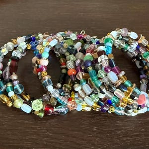 May include: A collection of beaded bracelets in various colors, including red, blue, green, and yellow. The bracelets are made with a variety of bead shapes and sizes, creating a textured and colorful accessory.