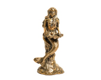May include: A gold-colored mermaid figurine with a pearl in her hand, sitting on a rock-like base.