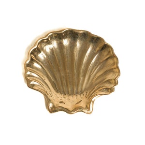 May include: A gold-colored seashell shaped dish. The dish is made of metal and has a smooth, shiny surface.