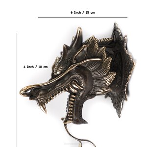 May include: A bronze dragon head sculpture with intricate details. The dragon's mouth is open, revealing sharp teeth. The sculpture is 6 inches tall and 4 inches wide.