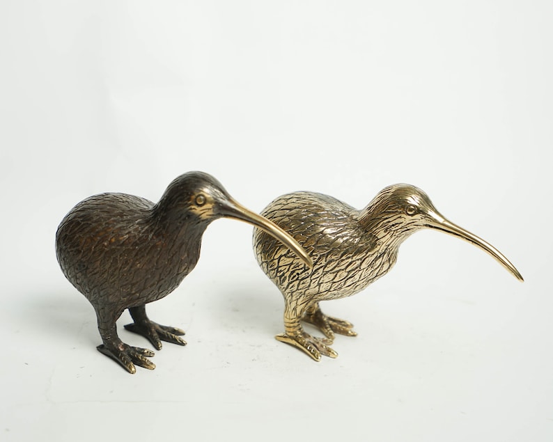 May include: Two bronze sculptures of kiwi birds. One is a dark brown color and the other is a gold color.