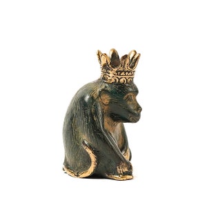 May include: A green bronze monkey figurine wearing a gold crown. The monkey is sitting with its head tilted to the side.