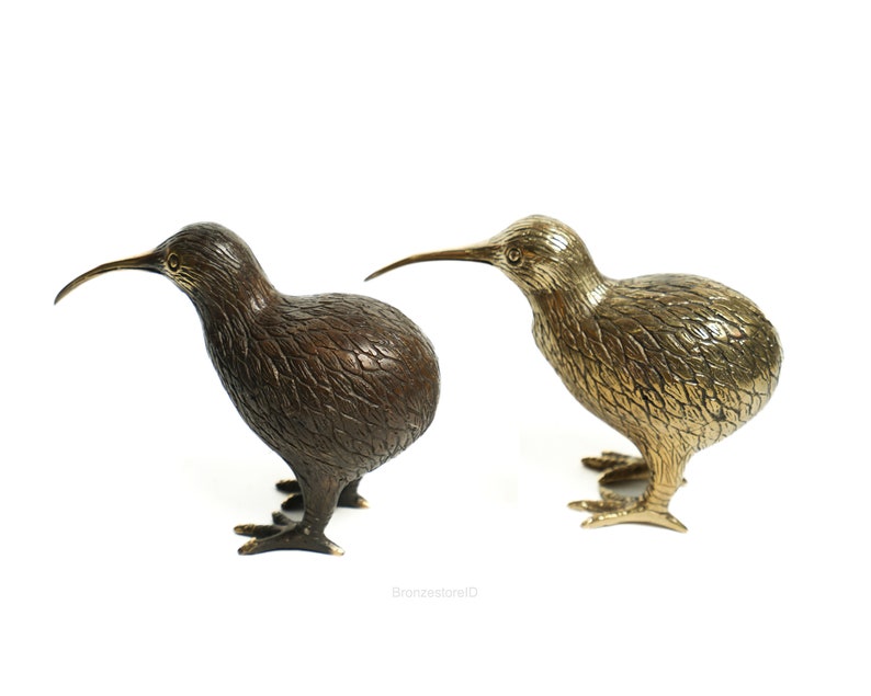 May include: Two bronze kiwi bird sculptures, one with a dark brown finish and the other with a gold finish. The sculptures are posed in a standing position with their beaks pointed forward.