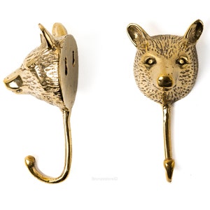 Puede incluir: Un gancho de pared de metal dorado en forma de cabeza de oso con un acabado texturizado. El gancho está diseñado para parecerse a una cabeza de oso con un gancho curvo que se extiende desde la parte inferior.