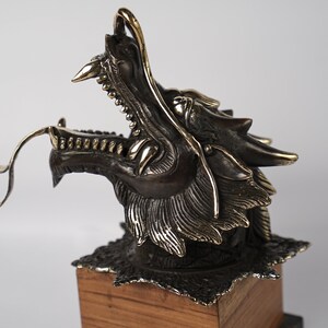May include: A bronze dragon head sculpture with gold accents, mounted on a wooden base.