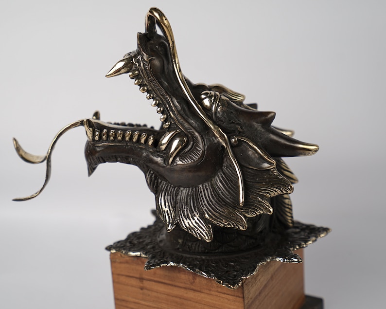 May include: A bronze dragon head sculpture with gold accents, mounted on a wooden base.