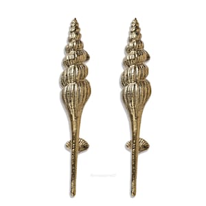 May include: A pair of gold-toned door handles shaped like seashells. The handles are detailed with ridges and swirls, giving them a realistic seashell appearance.