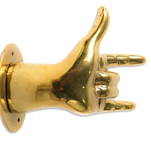 May include: A gold-colored metal hand sculpture in the shape of the "I love you" hand gesture. The hand is mounted on a round base.