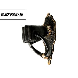 Puede incluir: Aldaba de puerta pulida en negro con un tirador en forma de pu&ntilde;o. La aldaba tiene una placa trasera ornamentada con detalles dorados y el texto "BLACK POLISHED". El tirador es un pu&ntilde;o y la aldaba est&aacute; montada sobre un fondo blanco.