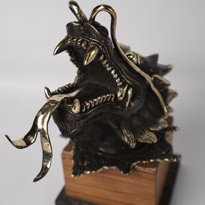 May include: A bronze dragon sculpture with a gold tongue and detailed scales. The dragon is mounted on a wooden base.